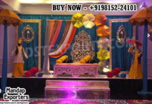 Vibrant Punjabi Theme Sangeet Stage With Punjabi Statues “Vibrant Punjabi Theme Sangeet Stage with colorful umbrellas, traditional Punjabi male and female statues, carved wedding sofa, sequin backdrop, and festive decor by DST Exporters.”