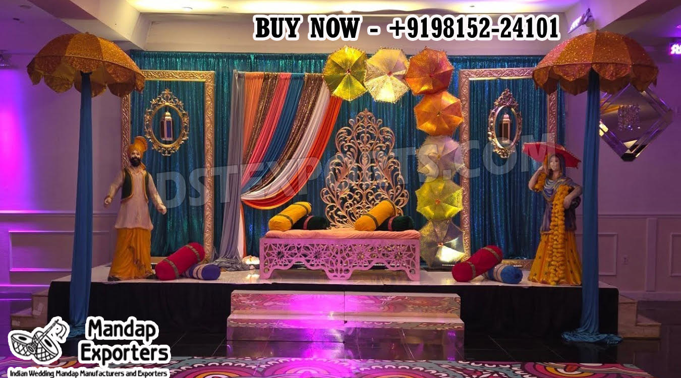 “Vibrant Punjabi Theme Sangeet Stage with colorful umbrellas, traditional Punjabi male and female statues, carved wedding sofa, sequin backdrop, and festive decor by DST Exporters.”
