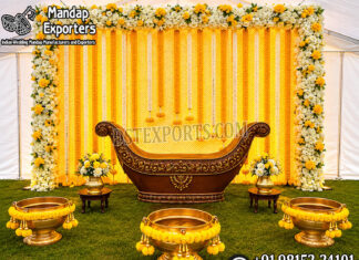 Outdoor Indian Wedding Pithi Ceremony Decor Setup Luxury outdoor Indian wedding pithi ceremony setup featuring a yellow floral backdrop, traditional decorative seating, brass urli bowls, flower arrangements, and festive haldi ceremony décor.