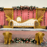 Elegant Indian wedding stage setup featuring a royal white and gold bridal sofa, ornate elephant carved panels, pink drapes, floral arrangements, and decorative elephant statues for traditional ceremonies.