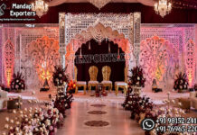 Trending Mirror Theme Mandap For Fusion Weddings Luxury fusion wedding mandap featuring ornate white mirror-style carved panels, decorative arches, elegant chandeliers, burgundy drapery, floral aisle décor, ambient lighting, and royal seating for bride and groom.