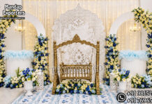 Top Selling Baby Cradle for Naming Ceremony Luxury gold baby cradle setup for naming ceremony featuring an ornate swing cradle, elegant white Mughal-style backdrop panel, floral arch frames decorated with blue and ivory flowers, hanging chandeliers, decorative flower stands, and premium baby welcome stage décor.