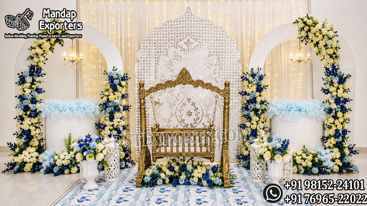 Luxury gold baby cradle setup for naming ceremony featuring an ornate swing cradle, elegant white Mughal-style backdrop panel, floral arch frames decorated with blue and ivory flowers, hanging chandeliers, decorative flower stands, and premium baby welcome stage décor.